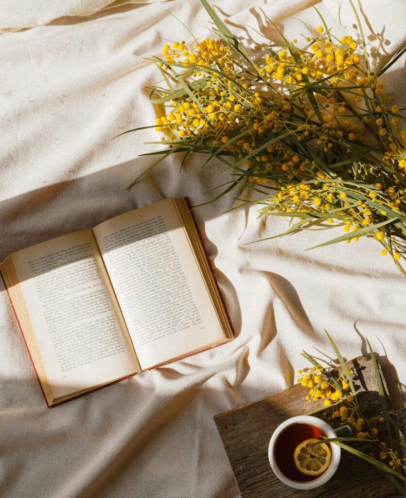 Relaxing scene with a book, cup of tea, and yellow flowers in warm sunlight.